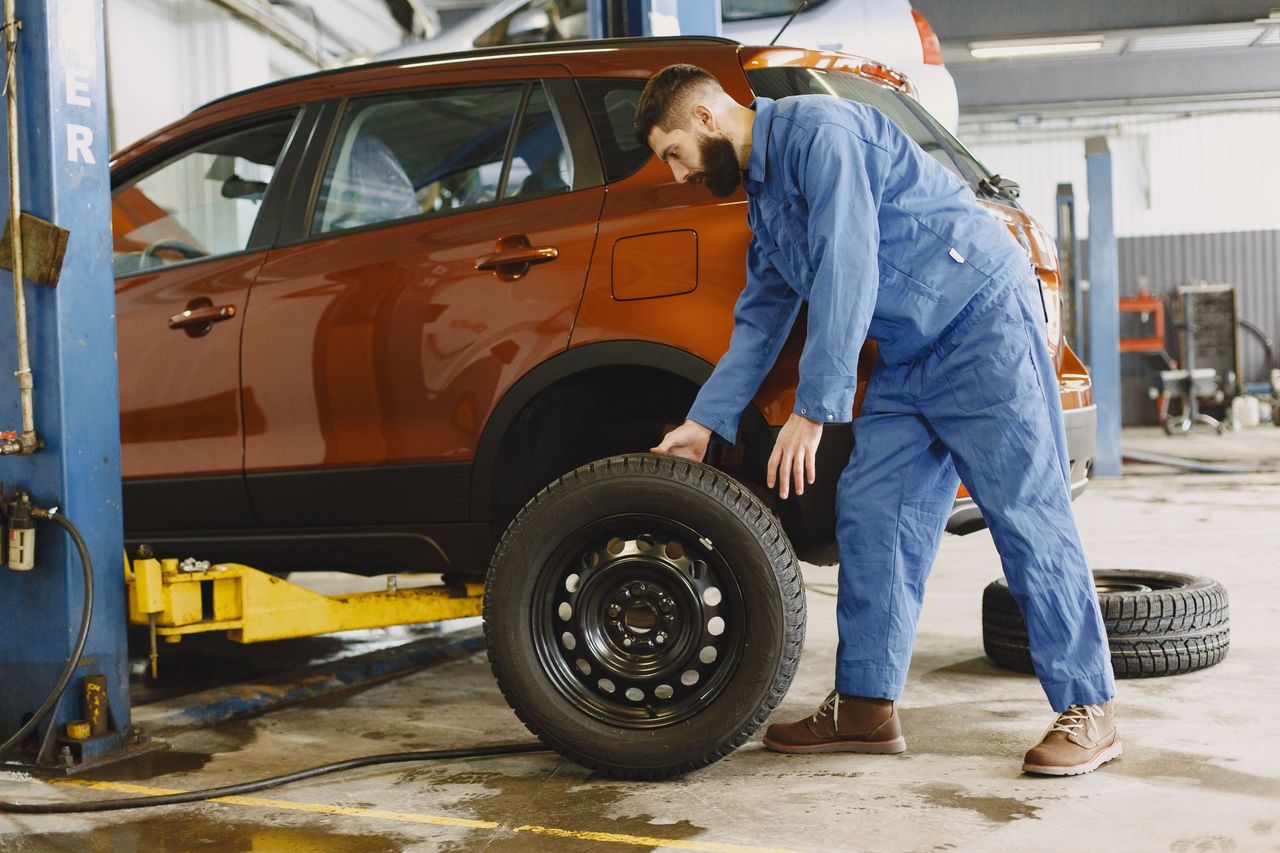 Technician moving a wheel beside an SUV on a lift in a tire service bay